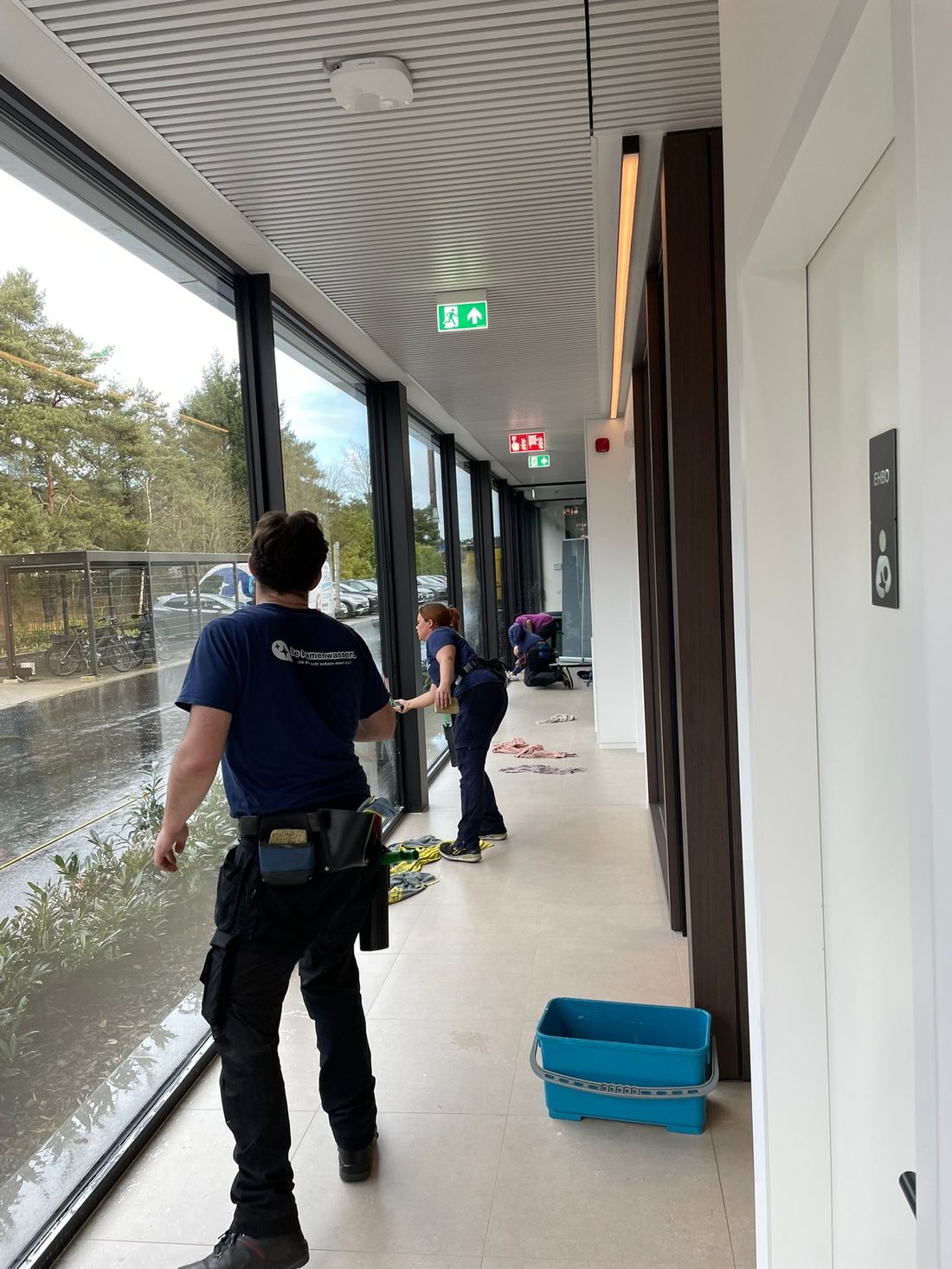 Twee medewerkers van De Ramenwassers wassen samen de ramen in een gang